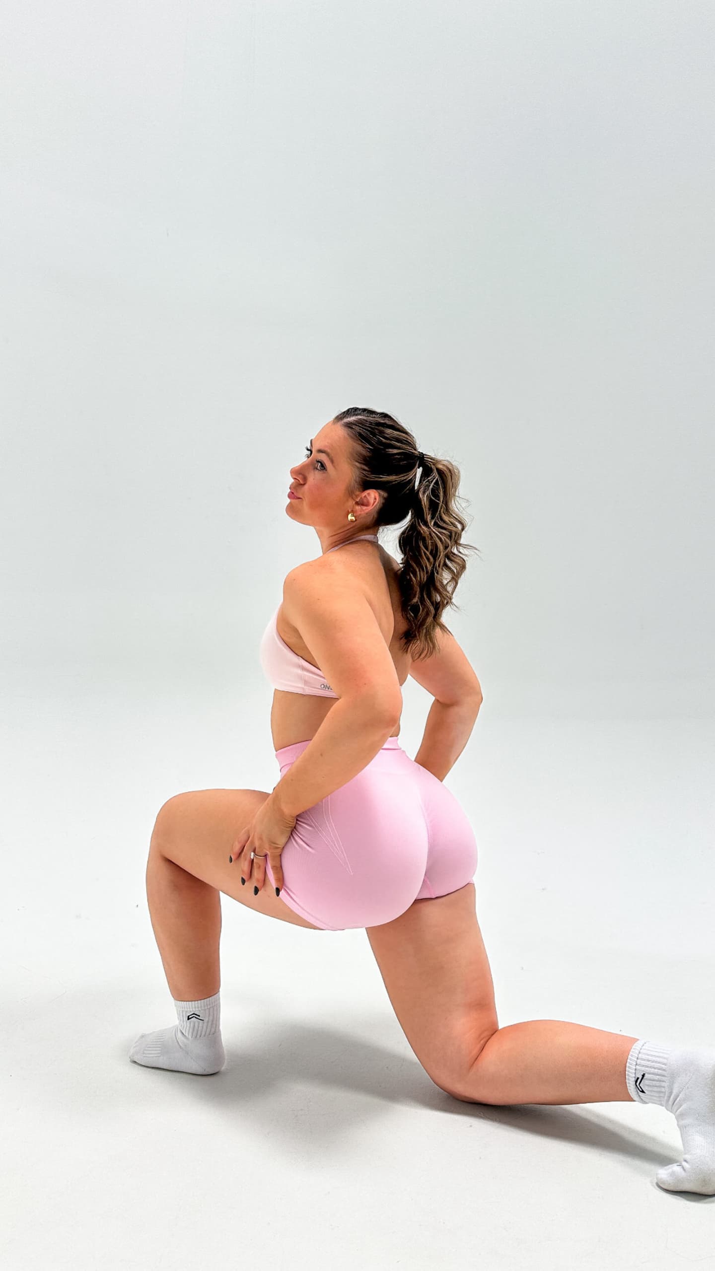 Cheyanne in a pink workout set, kneeling on one knee in a white studio